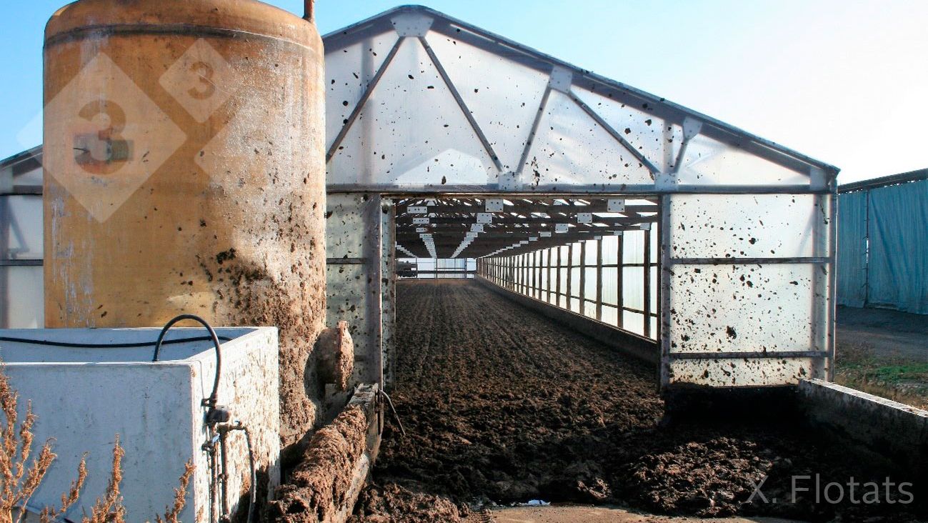 Figure 2. Picture of a solar drying system using a greenhouse. In the foreground is the acid tank and a biofilter for the treatment of gaseous emissions. (Courtesy of J. Soler, EMA depuraci&oacute;, Olot, Gerona)
